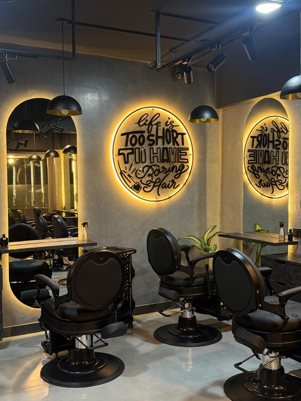 Styling stations with black barber chairs, arched mirrors and a lit sign reading "Life is too short to have boring hair" at The Man Redefined